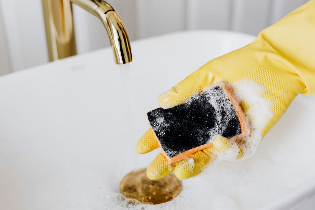 Gloved hand holding a soapy sponge over a bathroom basin