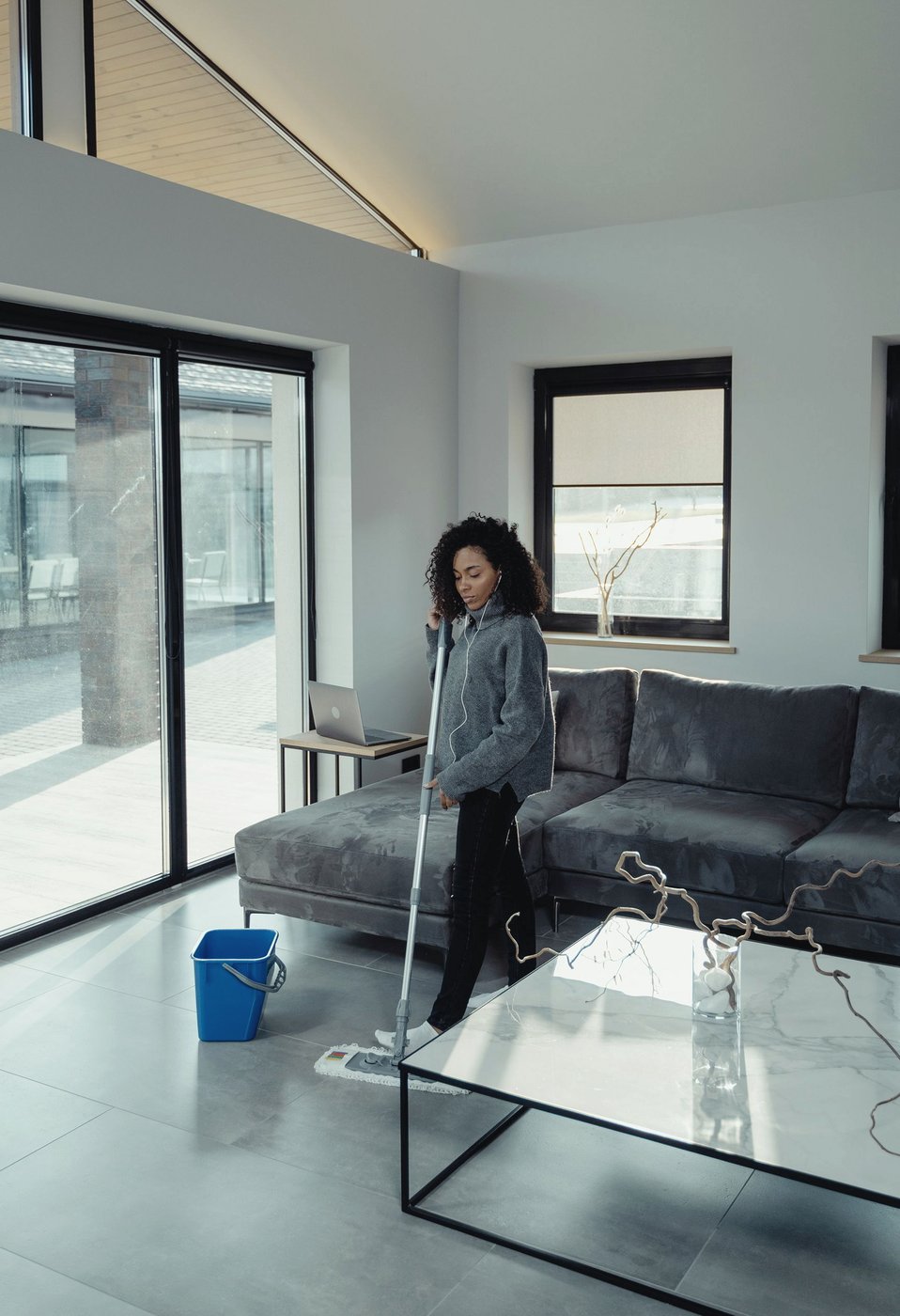Person mopping a tiled living room floor beside a sofa and coffee table